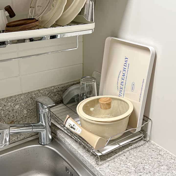 ベージュ調のキッチンシンクと食器乾燥棚に鍋とトレイが置かれた、清潔で効率的な印象の空間