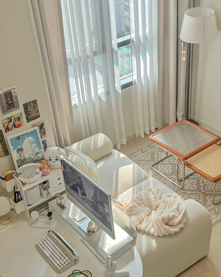 ホワイトとベージュのトーンで構成されたコンパクトなホームオフィス、白いソファとモニター、カーテンが配置された明るく居心地の良い空間