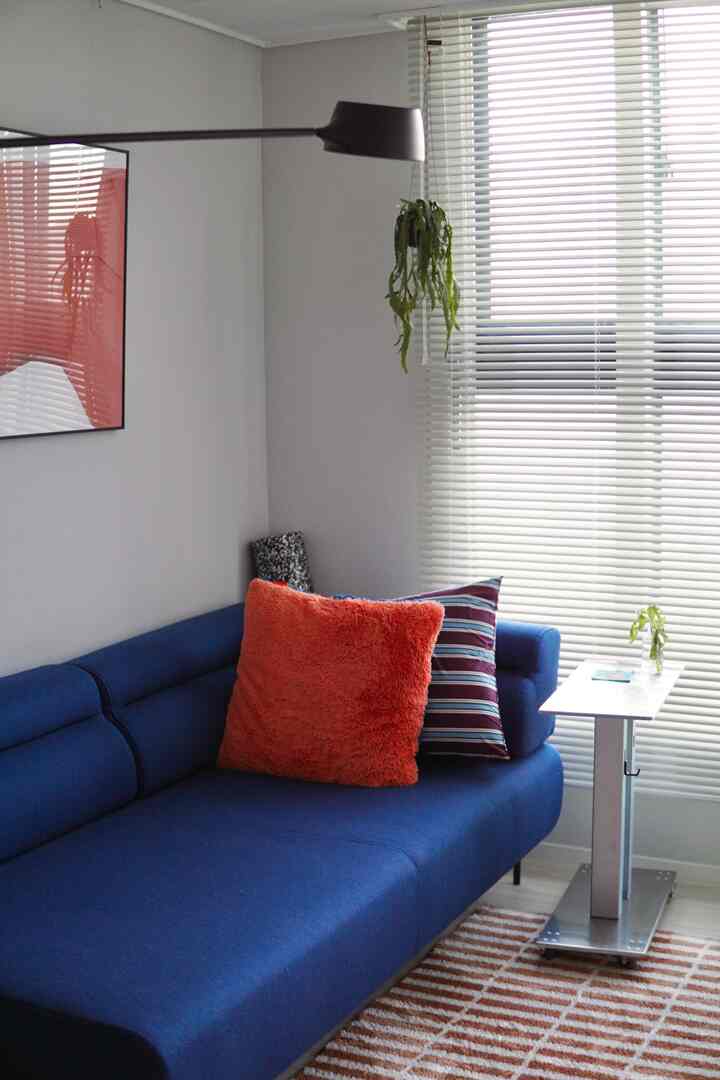 ネイビーのソファと赤いクッションがあるリビング、明るいアルミブラインドとモダンな雰囲気のインテリア