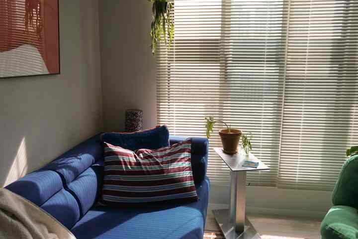 ホワイトのブラインドがかかったリビングの窓際に、ブルーのソファとストライプ柄のクッションが配置されたヴィンテージ感のあるインテリア