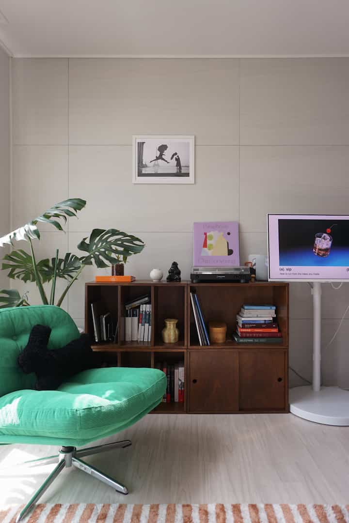 ブラウンの木製本棚とグリーンのアームチェアが配置されたシンプルで落ち着いた北欧風リビング