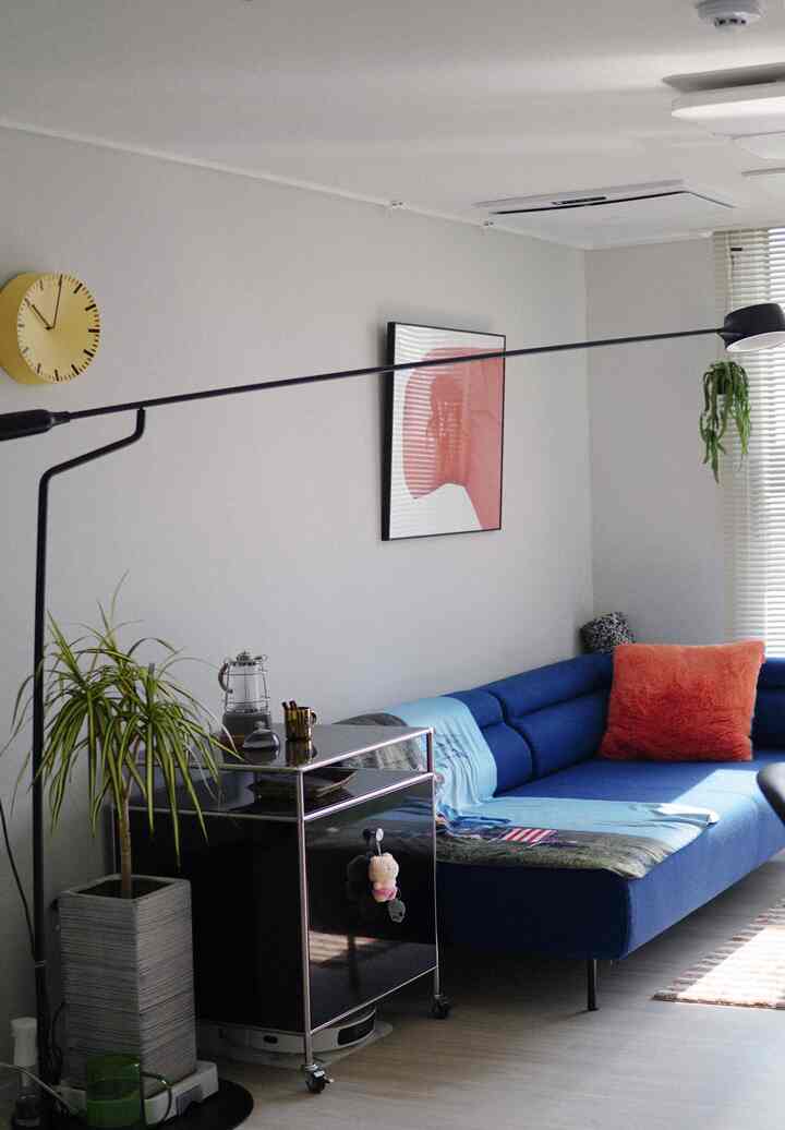 ホワイトトーンのリビングにネイビーのセクショナルソファとフロアランプ、植物と額縁が配置されたモダンで自然な雰囲気のインテリア