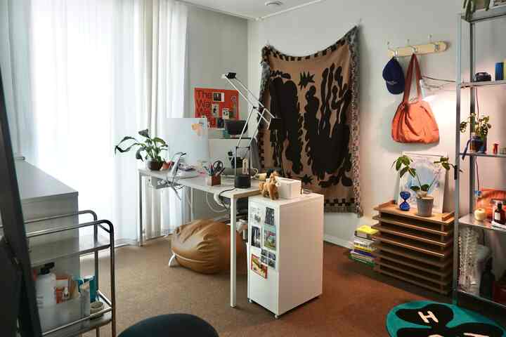 ナチュラルカラーの小さなホームオフィス、ホワイトデスクとブラウンのビーズクッション、植物が配置された雰囲気のある作業空間