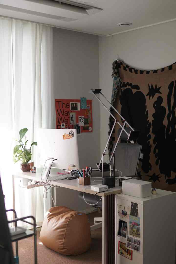 ナチュラルトーンのホームオフィス、中央にデスクとオフィスチェアがあり、左側に植物とビーンバッグが置かれた落ち着いた作業空間