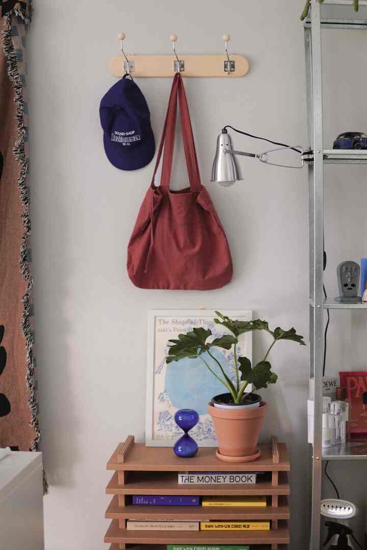 テラコッタのバッグとシルバーの壁灯、植物が置かれたウッドシェルフが配置されたナチュラルモダンな壁面インテリア