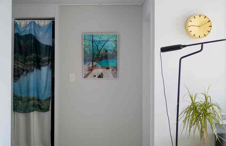 白い壁と青いカーテンのある玄関と廊下、壁に掛けられたポスターと黒いブラケットライトが配置されたモダンな空間