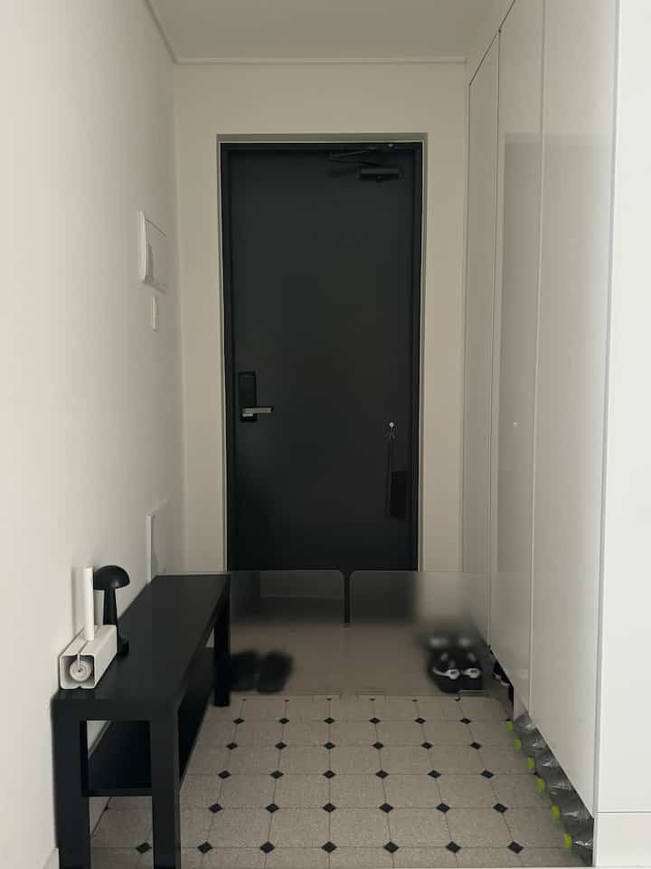 白と黒のトーンのモダンな玄関、左側にベンチ、右側にシューズラックが配置され、ペットのための透明な仕切りが設置されている印象的な空間