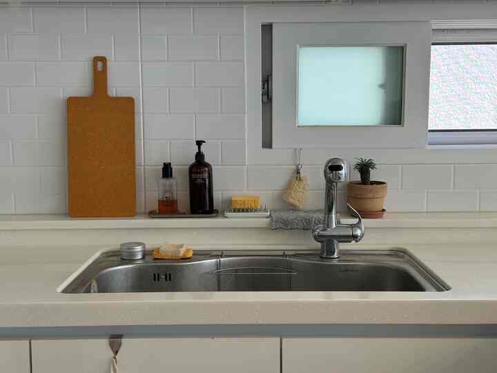 白いタイル壁のキッチン、ナチュラルカラーのシンクスペースにまな板と鉢植えが配置された落ち着いた印象の空間