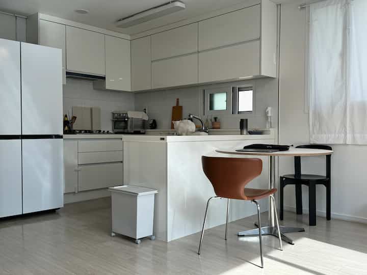 白とナチュラルカラーが調和したキッチン、キッチンアイランドと丸テーブル、猫がいる雰囲気のあるインテリア