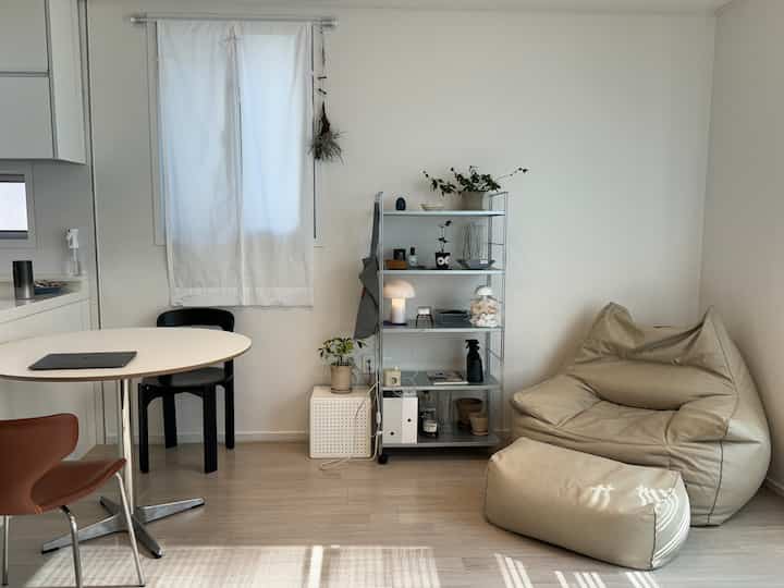 白とベージュのトーンの小さなリビング、ビーズクッションソファと棚が配置された自然でミニマルなインテリア