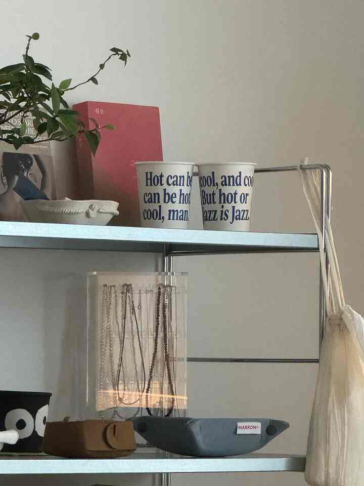 ベージュ色の壁とメタルシェルフ、アクリルのジュエリースタンドとカップが配置されたシンプルなインテリア空間