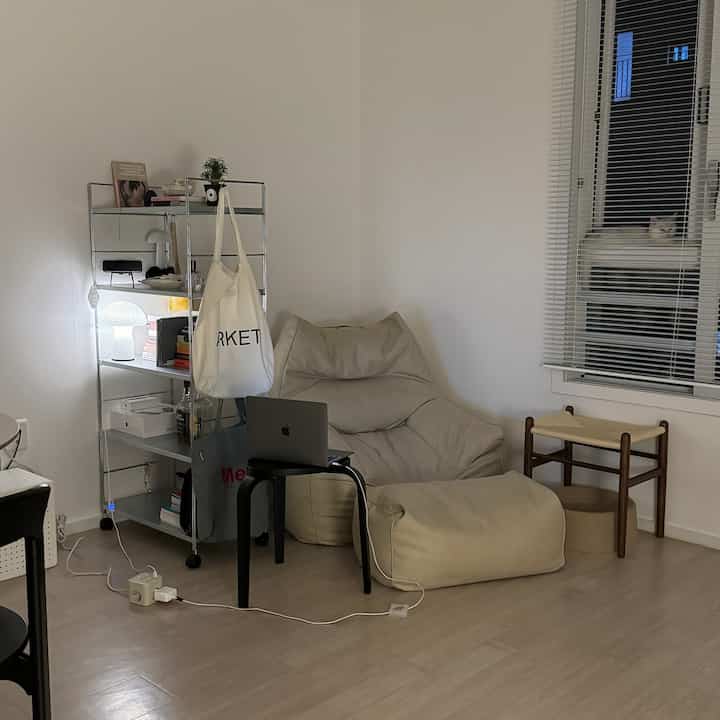 白い壁と木目調の床が調和した一人暮らし用のコンパクトなリビング、ベージュのビーズクッションとスツールが落ち着いた雰囲気を演出