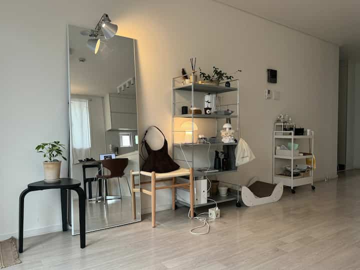 ナチュラルカラーのリビング、 大型の全身鏡と棚、スツールが配置されたモダンでワークスペースの雰囲気のあるインテリア