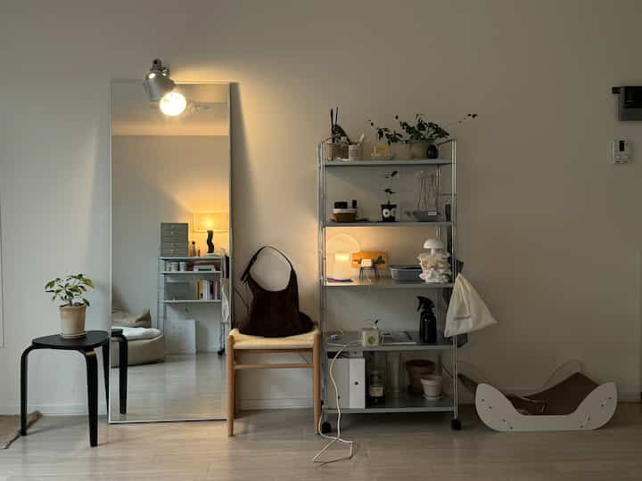 白い壁と木目調家具のリビング、壁掛け鏡とシルバーの金属棚、ビーンバッグソファと猫用爪とぎがある雰囲気のあるインテリア