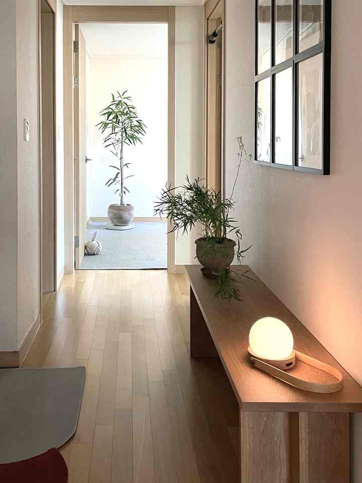 ナチュラルな木目調の玄関、木製ベンチの上に温かみのあるテーブルランプと植物が配置され、落ち着いた雰囲気のあるインテリア