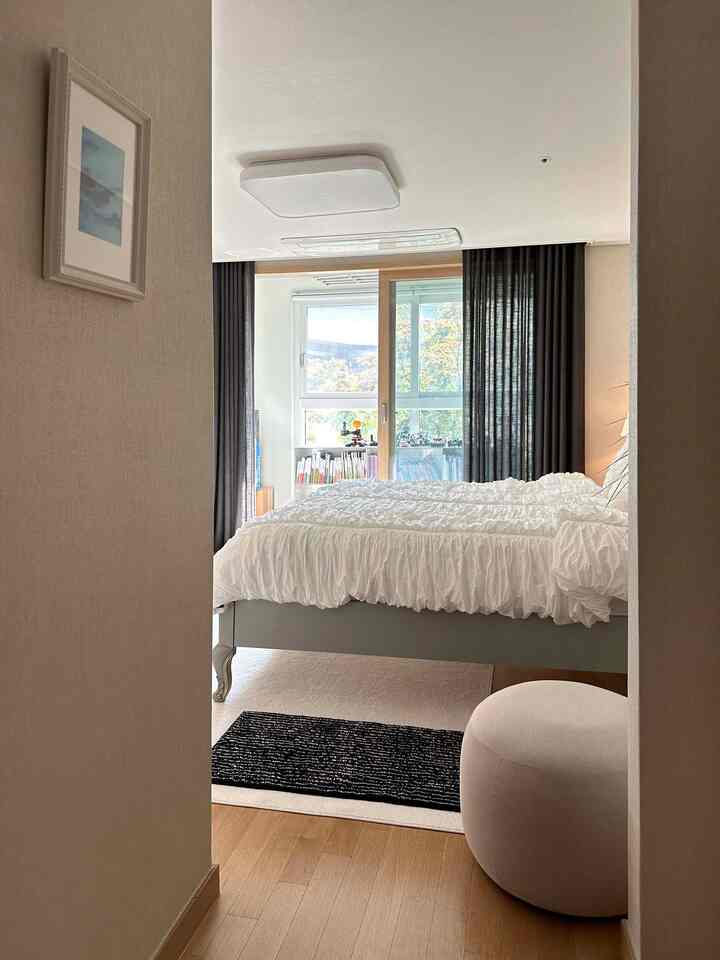 ホワイトの寝具とグレーのベッドフレーム、濃いカーテンが配置された明るくすっきりしたミニマルな寝室