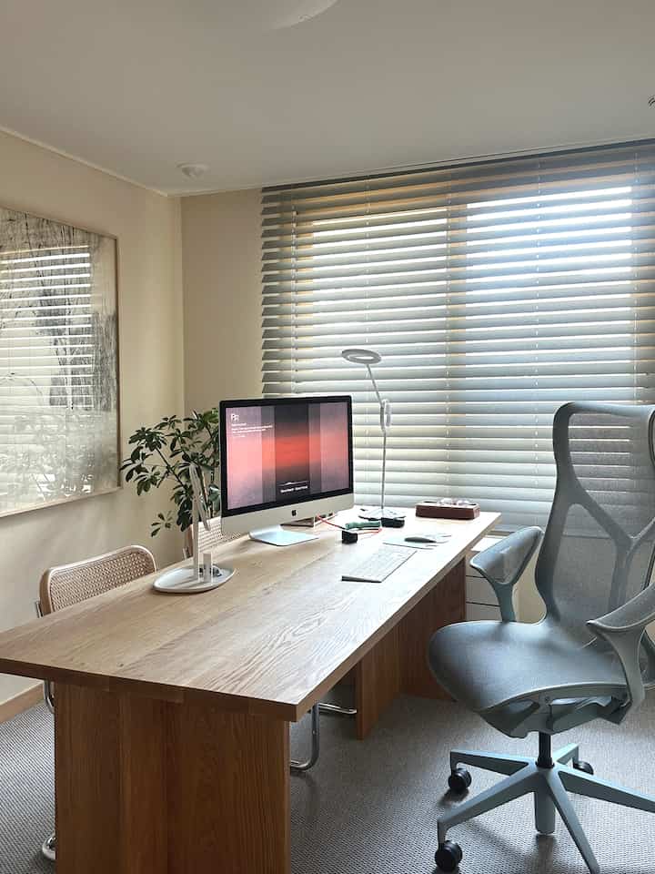 ナチュラルウッド調とグレーの色調のホームオフィス、広い木製デスクと人間工学的なオフィスチェアが配された清潔感ある作業空間