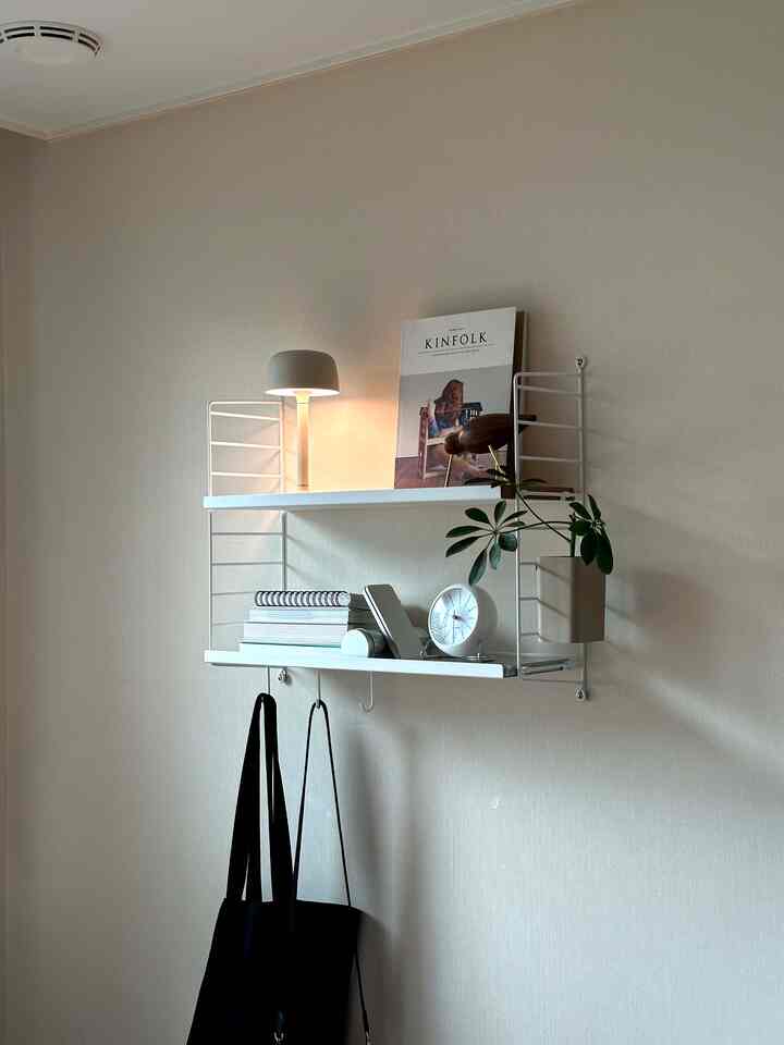 ホワイトトーンの壁に取り付けられた棚と照明が配置されたコンパクトな空間、棚の下にはバッグが掛けられた実用的なインテリア