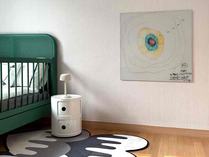 白い壁と緑の子供用ベッドが配置された子供部屋、子供の絵画とモノトーンのラグが印象的な空間