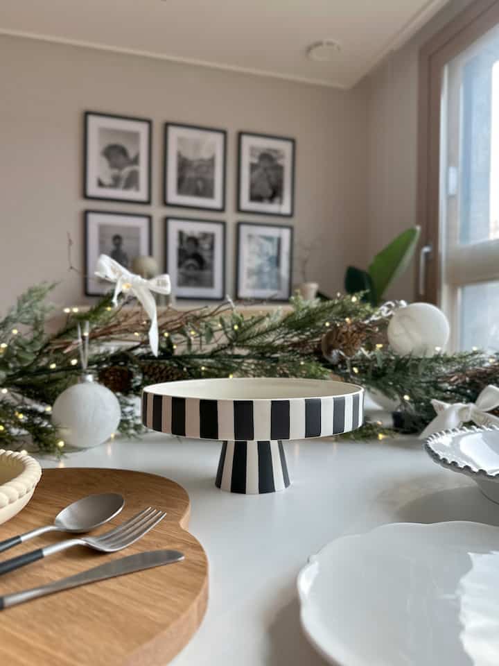 白と木目調が調和したダイニング空間、テーブルウェアとストライプ柄のケーキスタンドが配置された温かみのある雰囲気のインテリア