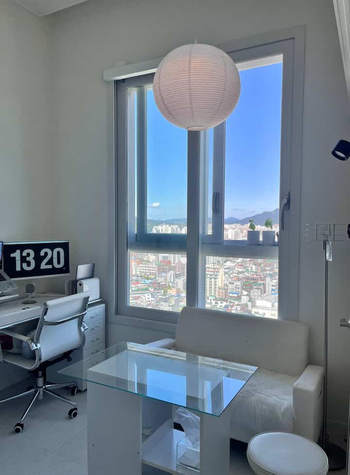 ホワイトカラーのナチュラルモダンなホームオフィス空間、大きな窓とソファ、デスク、椅子が配置された清潔感のある室内