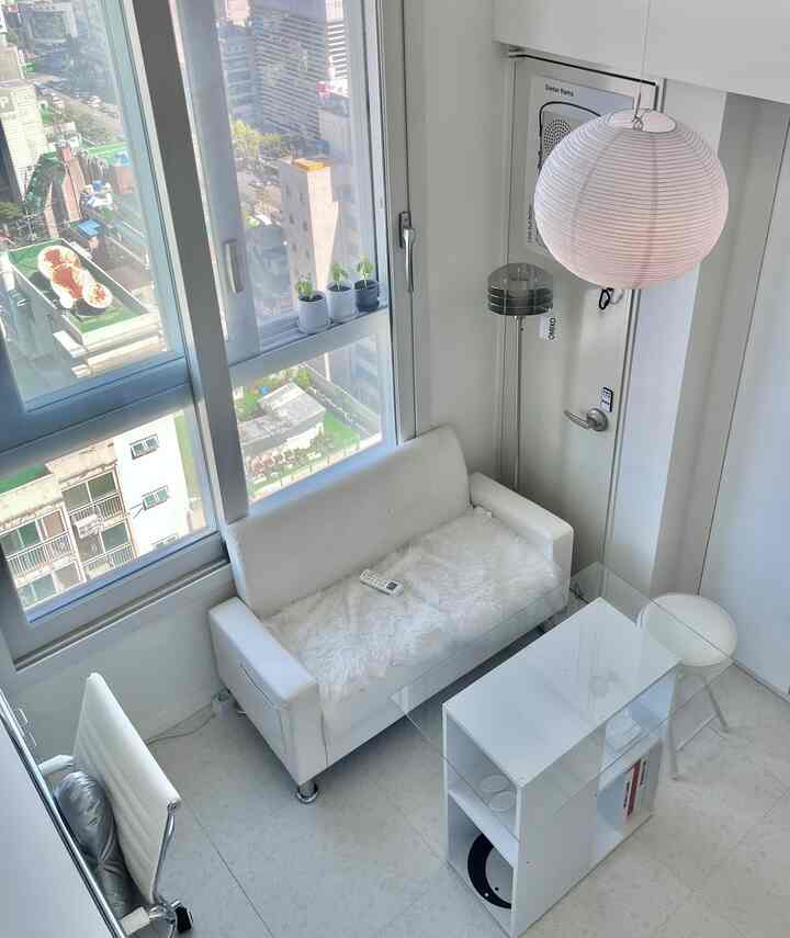 白を基調とした狭い1階のリビング、コンパクトな2人用ソファとガラステーブル、フロアランプが配置されたミニマルなインテリア