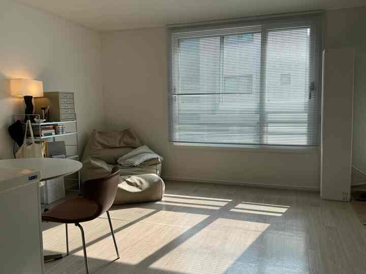 明るいホワイトトーンのモダンなリビング、ブラインドの大きな窓、ベージュのビーンバッグとブラウンのダイニングチェアが配置された清潔感ある空間