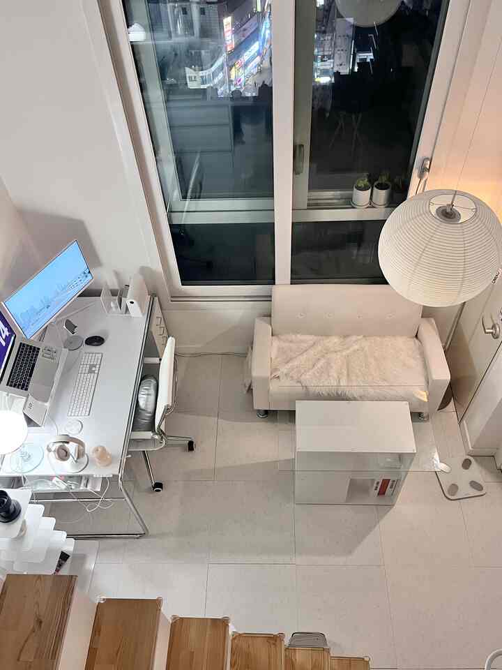 ホワイトとウッドトーンの一人暮らしリビング兼ホームオフィス、シンプルでモダンな作業スペースとソファが配置された印象的な空間