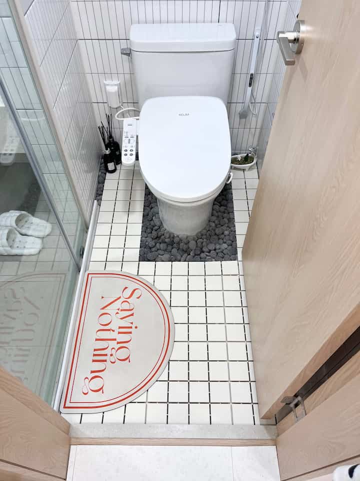 清潔な白いタイル床と黒い石ころのあるドライトイレ空間、シャワー室と分離された実用的なインテリア