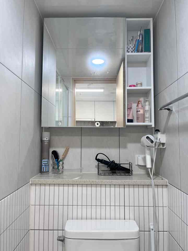 白を基調とした清潔感のあるトイレ、鏡付き収納キャビネットとドライヤーホルダーを備えた機能的なインテリア