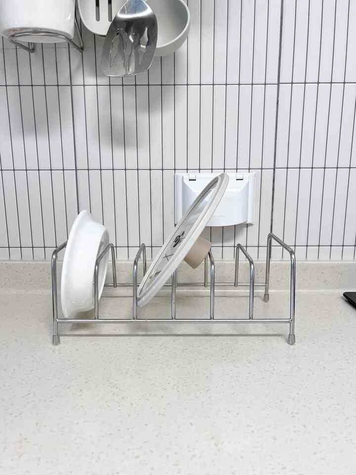 白いタイル壁と調理台のあるキッチン、ステンレスの皿立てに皿と蓋が整然と並べられたモダンなインテリア