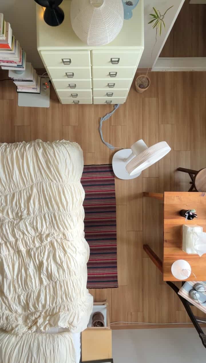 アイボリー色調の寝室、ベッドとデスク、扇風機が配置されたナチュラルで落ち着いた雰囲気のインテリア