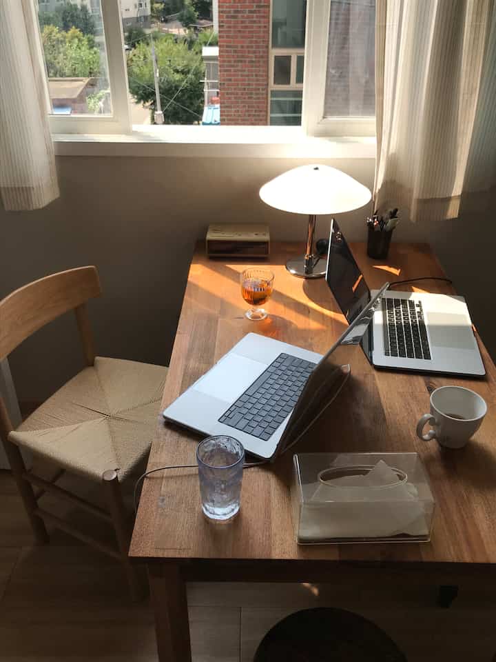 自然光が差し込む木目調のホームオフィス空間、二人用デスクと椅子が配置された落ち着いた作業スペース