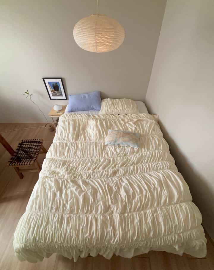 アイボリーとホワイトのトーンの寝室、シャーリングディテールの掛け布団カバーと木製ナイトテーブルが配置されたナチュラルでシンプルな空間