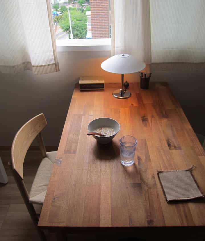 温かみのあるウッドトーンのダイニングテーブルとラタンチェアが配置され、ベージュのカーテンが窓辺を飾る印象的な空間