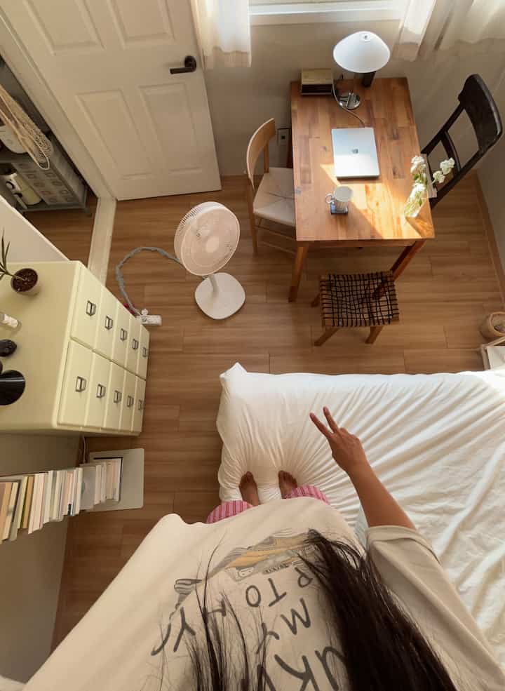 ホワイトとウッドトーンのコンパクトな寝室、机とスツールが配置された清潔で居心地の良い空間