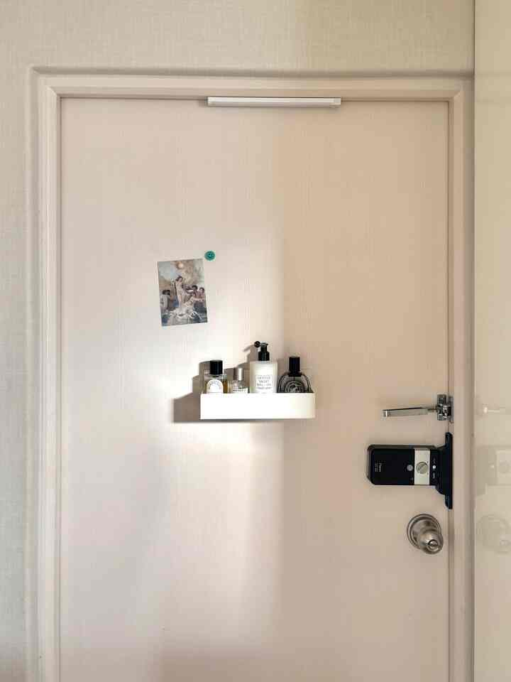 明るいホワイトトーンの玄関の扉に強力な磁石棚が設置され、香水とデジタルドアロックが配置された実用的な空間