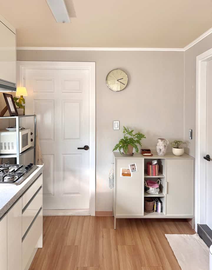 ベージュとホワイトのウッド調キッチン、整頓されたキャビネットが配置されたミニマルで落ち着いた雰囲気の空間