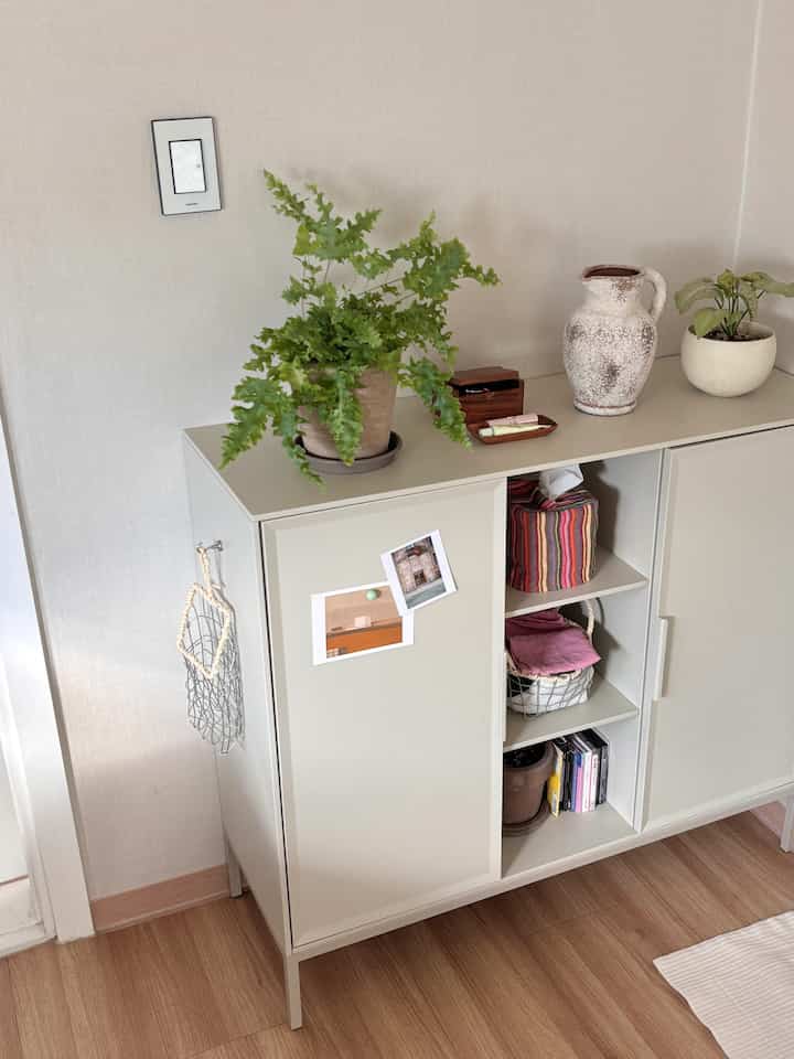 ベージュ色の壁と木の床を持つナチュラルな玄関スペース、収納キャビネットや植物、飾り物が配置され、落ち着いた雰囲気のインテリア