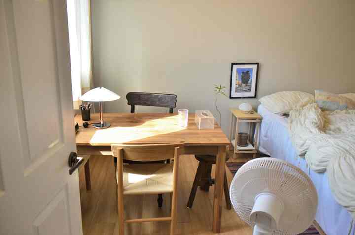 ナチュラルな木目調と白色が調和する一人暮らしの寝室、木製デスクとナイトテーブルが配置された温かみのある空間