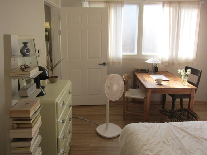 温かみのあるベージュと木目調の寝室、アイボリーのカーテンが窓にかかり、木製のデスクとドレッサーが配置された自然なインテリア