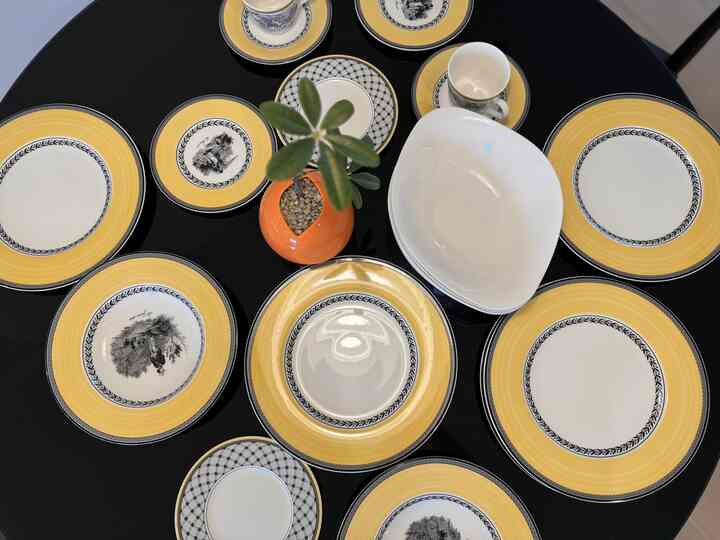 黒いダイニングテーブルの上に黄色の縁取りがされたビレロイ＆ボッホのアウデンシリーズの皿と白いボウル、オレンジ色の鉢植えが置かれた調理スペースのインテリア