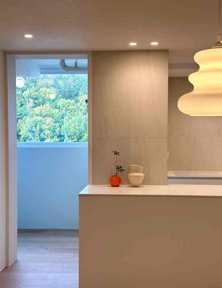 白とナチュラルトーンのキッチンスペース、窓越しに自然の風景が額縁のように広がる印象的なインテリア