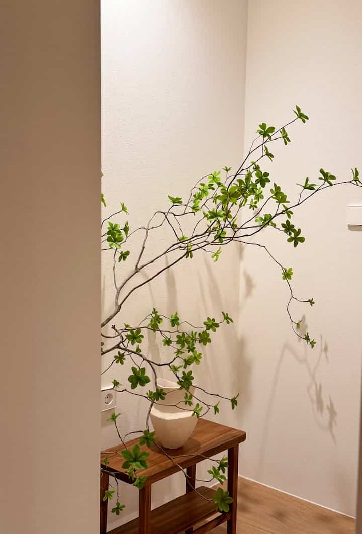 ナチュラルカラーの玄関、アカシアウッドのベンチの上に緑の葉が豊かな枝が置かれた清潔で落ち着いた雰囲気のインテリア