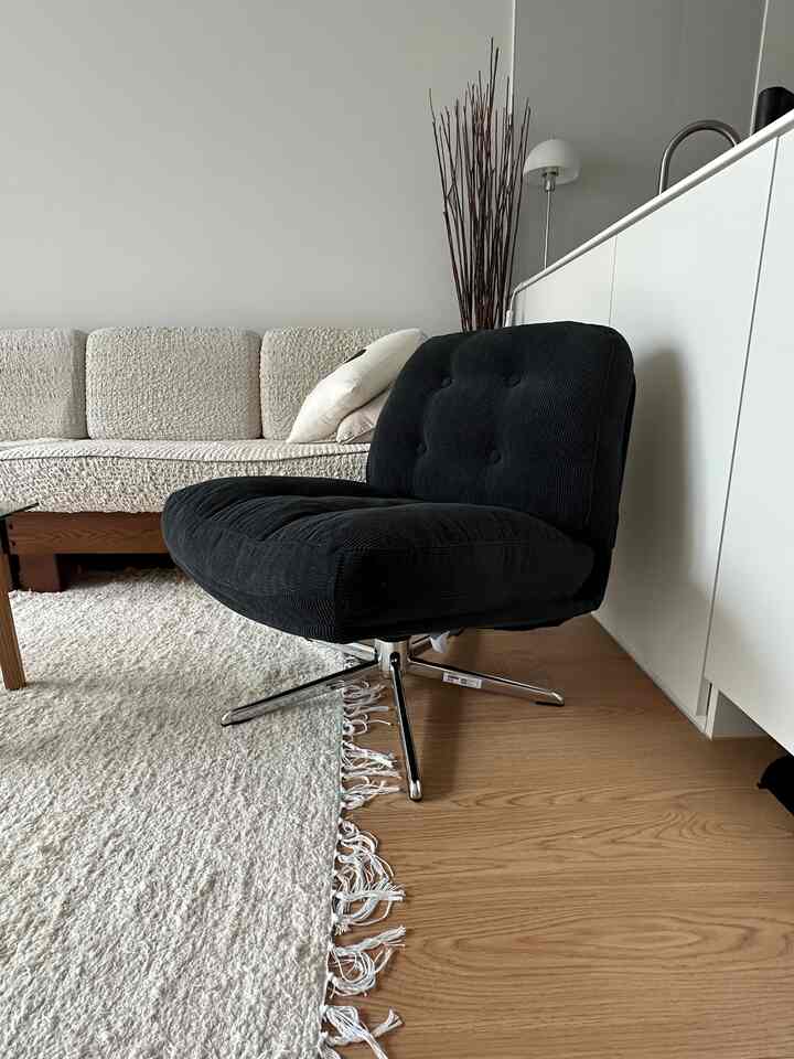 ナチュラルカラーの木目調フロアとクリーム色のラグがあるリビング、黒いコーデュロイスイベルアームチェアが配置された居心地の良い空間