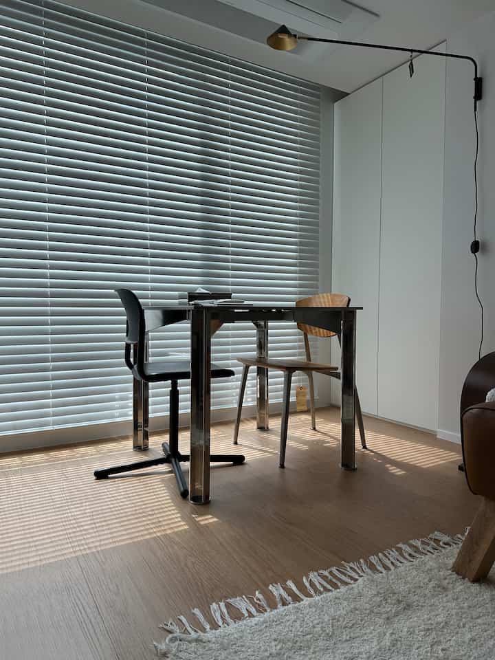 ホワイトとブラウンのナチュラルトーンが印象的なミニマルなホームオフィス兼ダイニングスペース、アルミニウム脚のヴィンテージテーブルと二脚の椅子が配置されたすっきりとしたインテリア