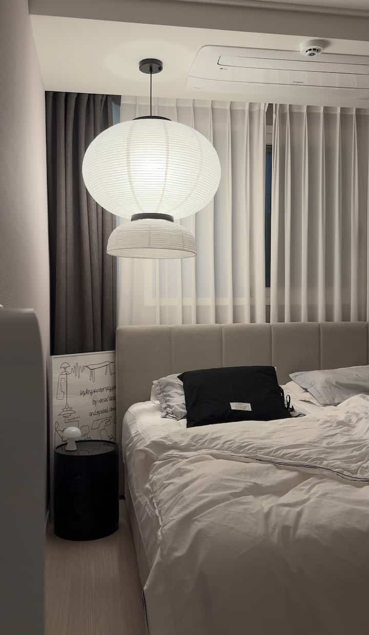 白と黒の調和が取れた寝室、ペンダントライトとカーテンが際立つモダンな雰囲気のインテリア