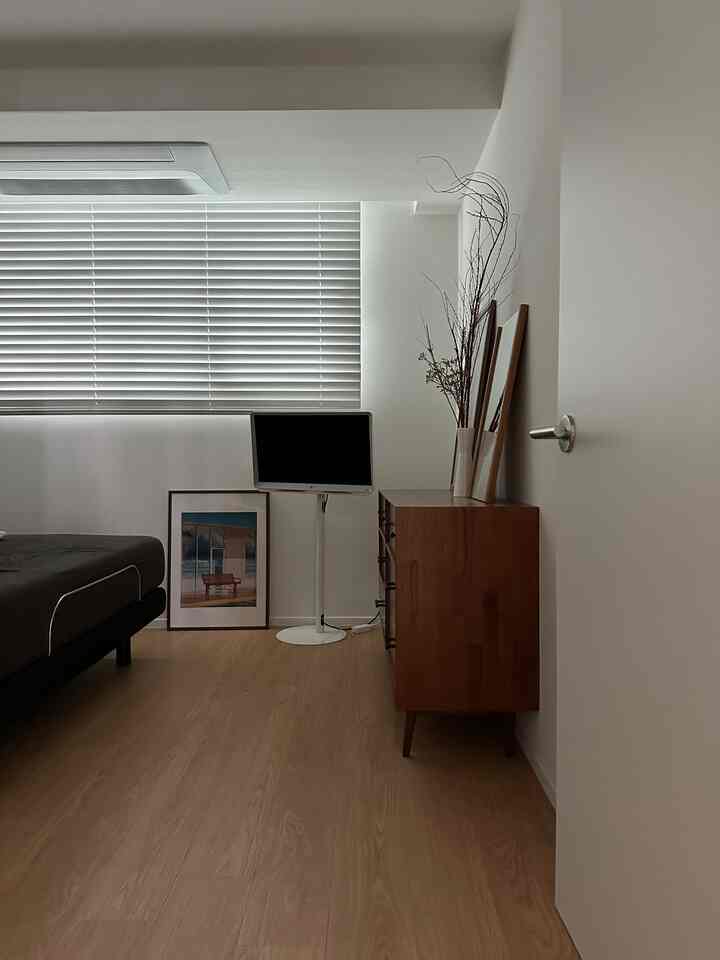 ナチュラルなベージュとホワイトの色調の寝室、モーションベッドとテレビ台、木製の化粧台と鏡が配置されたシンプルなインテリア