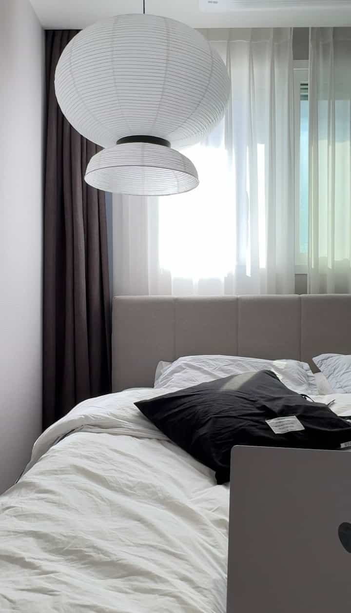 白と黒のモノトーンの寝室、グレーのファブリックベッドフレームと大きなペンダントライトが配置された落ち着いたインテリア