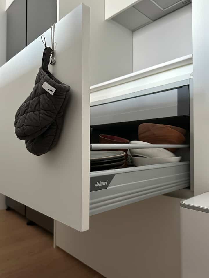 ホワイトの引き出しと木目調の床が調和するキッチンの収納引き出し、スムーズに開いたブルム製引き出しが特徴的。